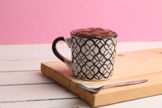 Selektiver Fokusschuss einer Tasse heißer Schokolade auf einem Holzbrett mit einem rosa Hintergrund