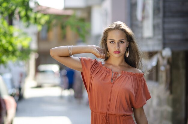 Selektiver Fokusschuss eines weiblichen Modells in einem rot-orangefarbenen Kleid in einer Gasse mit einem verschwommenen Hintergrund