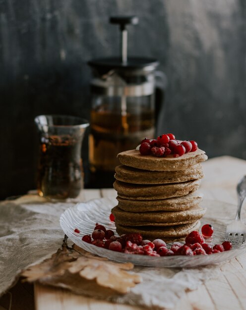 Selektiver Nahaufnahmeschuss eines Stapels Pfannkuchen mit roten Beeren auf einem Teller nahe einem Teekanne