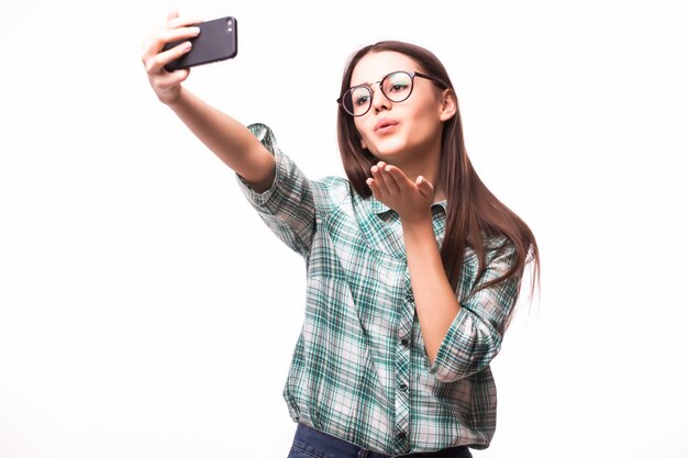 Selfie .. Attraktive junge Frau, die Handy hält und Foto von sich selbst macht, während sie gegen Weiß steht