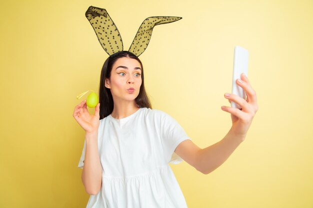 Selfie machen. Kaukasische Frau als Osterhase auf gelbem Hintergrund.