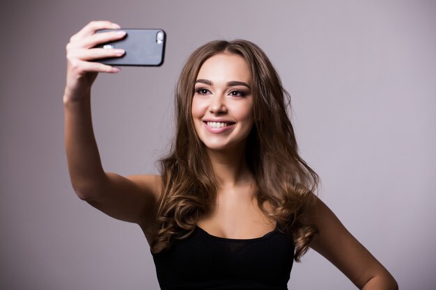 Selfie Zeit. Freudige junge Frauen, die Selfie durch ihr Smartphone auf grauer Wand machen