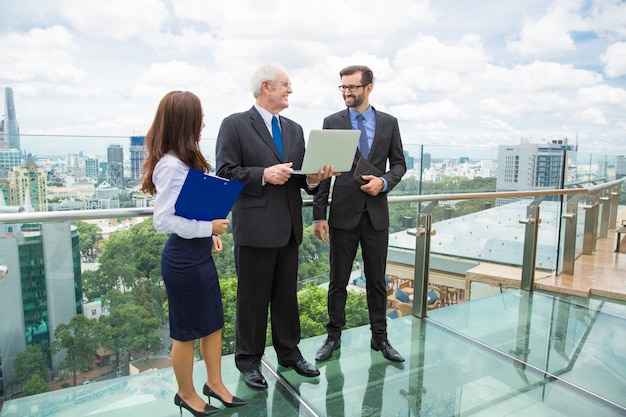 Senior Business Mann mit einem Laptop zu zwei anderen Arbeitern sprechen