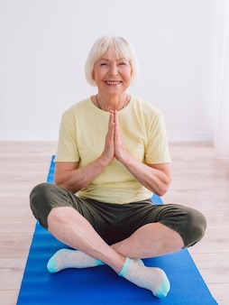 Senior fröhliche friedliche frau macht yoga indoor namaste hände anti-age-sport-yoga-konzept