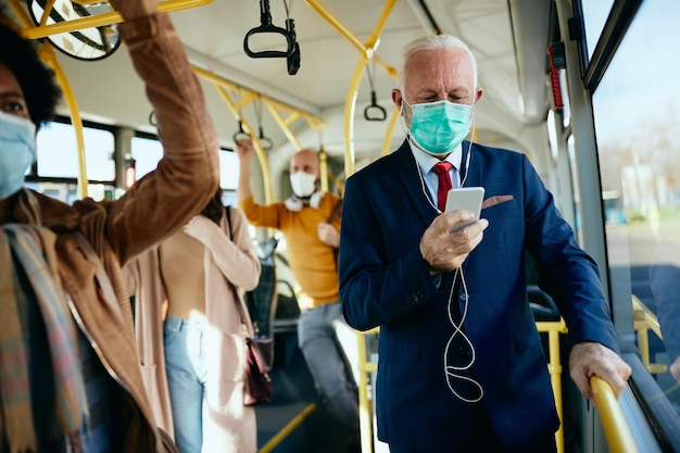 Senior geschäftsmann mit gesichtsmaske mit smartphone in öffentlichen verkehrsmitteln