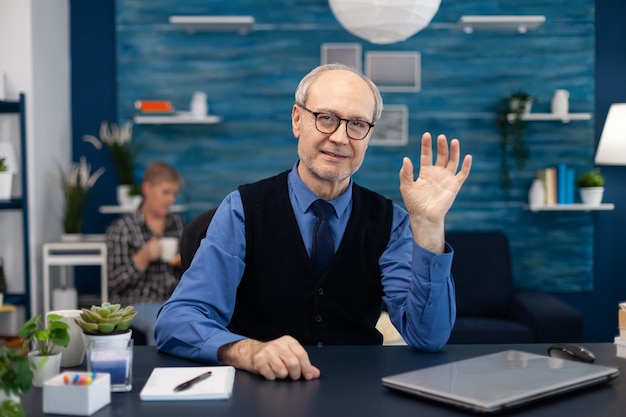 Senior Geschäftsmann winkt mit Brille während des Videoanrufs in die Kamera