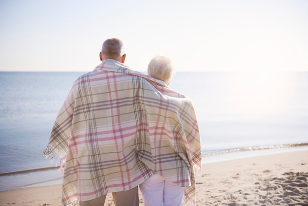 Senioren stehen bedeckt mit warmer Decke im Strand