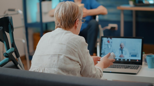 Seniorentreffen mit Spezialisten für Online-Telemedizin-Anrufe mit Laptop-Computer. Rentnerin, die mit einem Sanitäter über eine Ferntelefonkonferenz für Telemedizin spricht. Internetberatung.