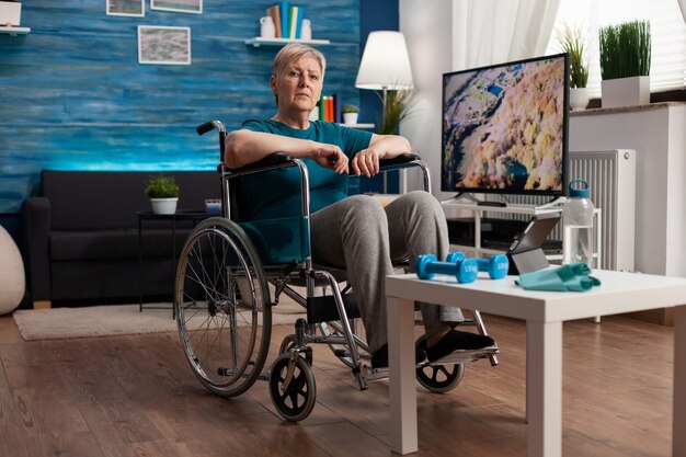 Seniorin mit Behinderung im Rollstuhl, die auf einem Tablet-Computer gymnastisches Online-Video anschaut
