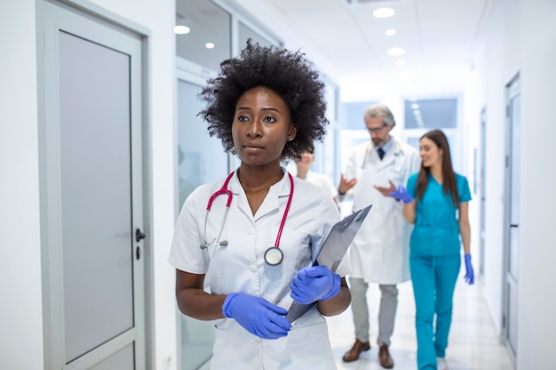 Seriöse afroamerikanische Ärztin, die mit den Testergebnissen des Patienten spazieren geht, bevor sie sich mit dem Patienten trifft Der Arzt befindet sich in einem Krankenhausflur