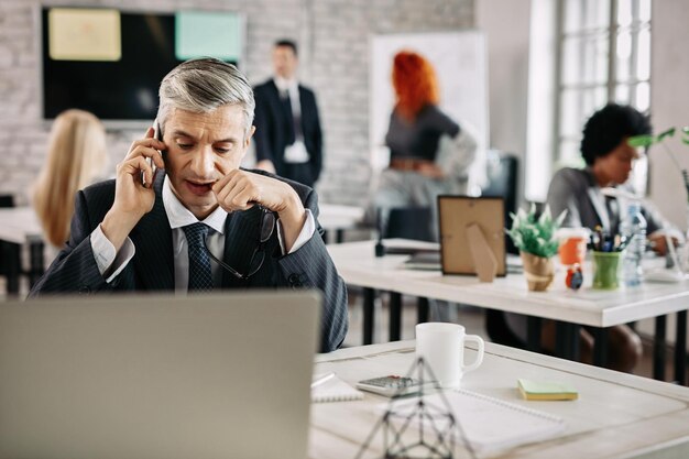 Seriöser Geschäftsmann, der am Schreibtisch im Büro sitzt und mit jemandem am Handy spricht