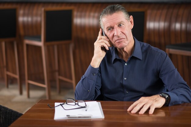 Serious älterer Mann am Telefon sprechen in Restaurant