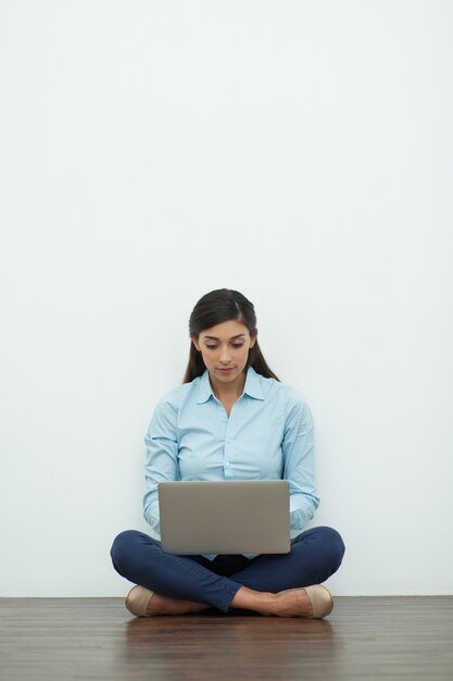 Serious junge Frau auf Laptop auf dem Boden