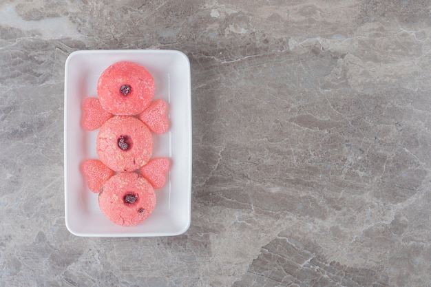 Servieren von rosa Keksen und Geleebonbons auf einer Platte auf Marmoroberfläche