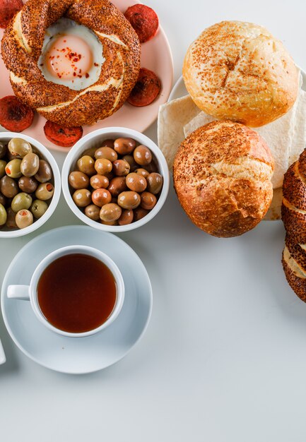 Set einer Tasse Tee, türkischer Bagel, Oliven, Brot und Eier mit Wurst in einem Teller auf einer weißen Oberfläche