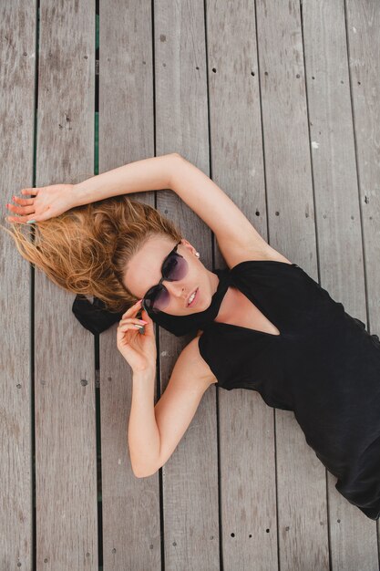 Sexy attraktive Luxusfrau gekleidet im schwarzen Kleid, das auf dem Boden liegend trägt Sonnenbrille, Sommerferien, Ansicht von oben