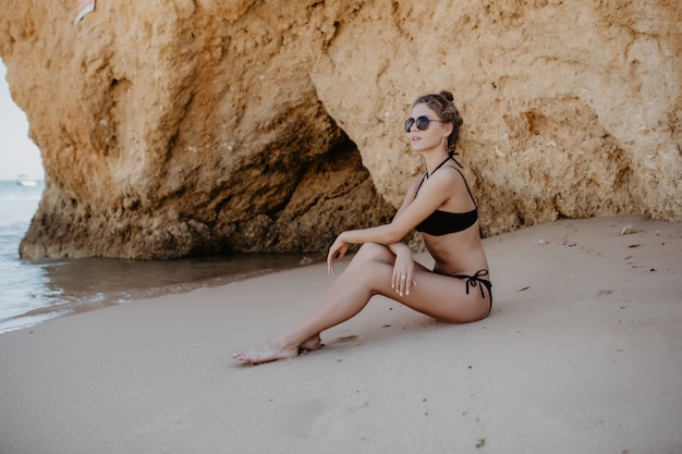 Sexy blondes Mädchen im schwarzen Bikini, der auf einem Strand aufwirft