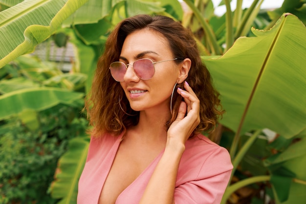 Sexy europäische Frau mit den lockigen Haaren im rosa Kleid, das über Palmen steht.