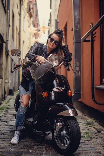 Sexy Frau in Blue Jeans und Lederjacke sitzt auf Roller in der Altstadt.