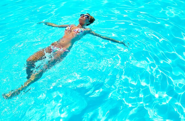 sexy heißes schönes Mädchenmodell mit dunklem Haar in der bunten Badebekleidung, die auf Rücken schwimmt