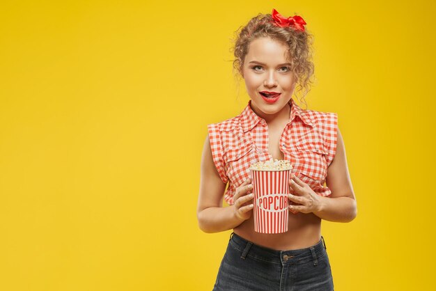 Sexy Mädchen mit roter Schleife des gelockten Haares, die Popcorneimer hält