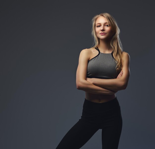 Sexy schlankes blondes Mädchen in Sportkleidung posiert in einem Studio. Isoliert auf grauem Hintergrund.