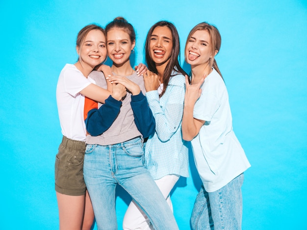 Sexy sorglose Frauen, die nahe blauer Wand im Studio aufwerfen. Positive Modelle, die Spaß haben und umarmen. Sie zeigen Zungen