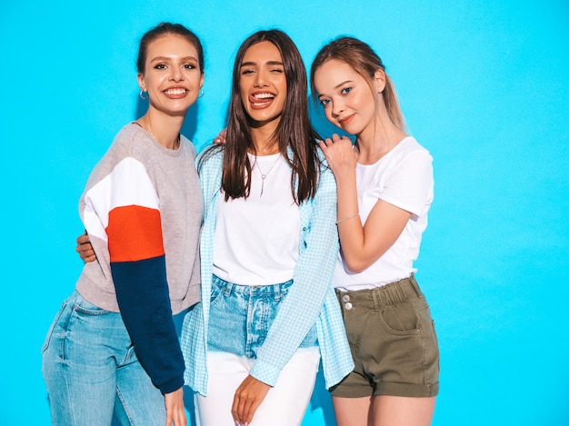 Sexy sorglose frauen, die nahe blauer wand im studio aufwerfen. positive models, die spaß haben und umarmen