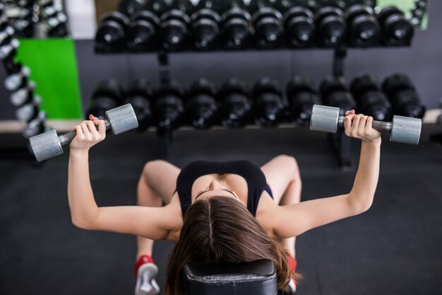 Sexy sportliche muskulöse junge Frau, die mit zwei silbernen Hanteln ausarbeitet