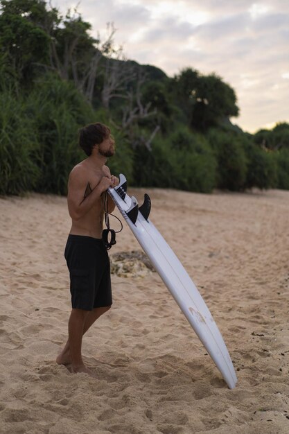 Kostenloses Foto sexy surfer, der mann mit surfbrett surft. hübscher junger männlicher athlet, der surfbrett mit nassen haaren im sommerstrandsporturlaub hält. reiseziel für sportreisen. surfer-lebensstil.