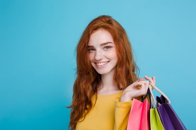 Shopping Concept - Close up Portrait junge schöne attraktive Redhair Mädchen lächelnd Blick auf Kamera mit Einkaufstasche. Blauer Pastellhintergrund. Platz kopieren