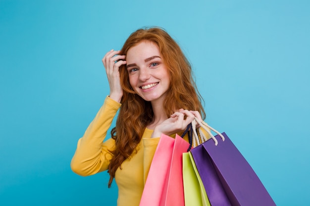 Shopping Concept - Close up Portrait junge schöne attraktive Redhair Mädchen lächelnd Blick auf Kamera mit Einkaufstasche. Blauer Pastellhintergrund. Platz kopieren