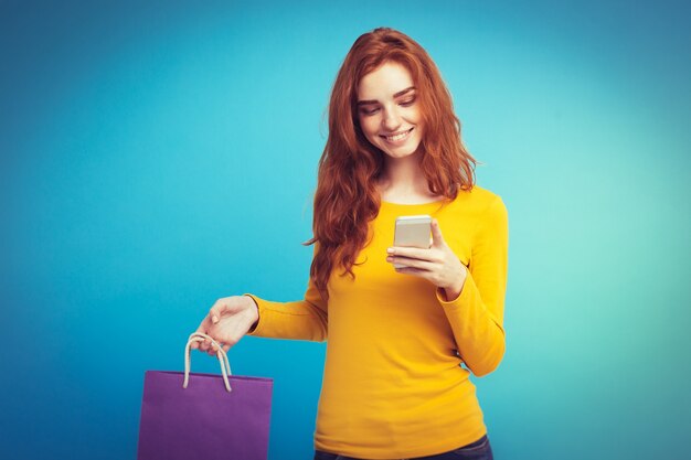 Shopping Concept - Close up Portrait junge schöne attraktive Redhair Mädchen lächelnd Blick auf Kamera mit Einkaufstasche. Blauer Pastellhintergrund. Platz kopieren