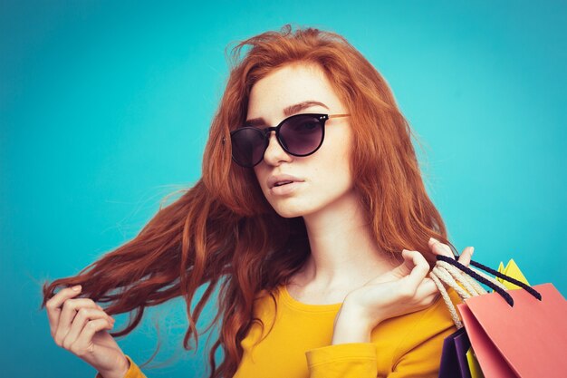 Shopping Concept - Close up Portrait junge schöne attraktive Redhair Mädchen lächelnd Blick auf Kamera mit Einkaufstasche. Blauer Pastellhintergrund. Platz kopieren