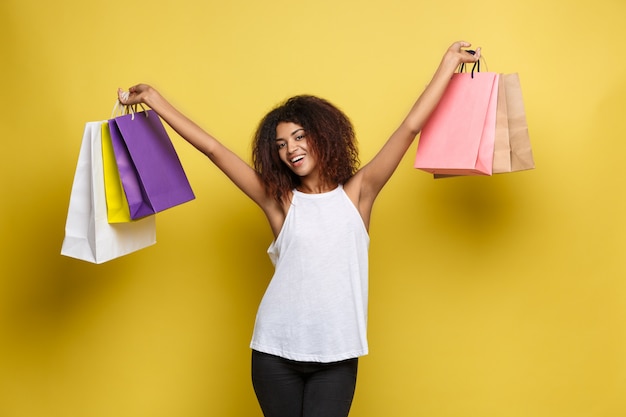 Shopping-konzept - close up portrait junge schöne attraktive afrikanische frau lächelnd und freudig mit bunten einkaufstasche. gelbe pastellwand hintergrund. text kopieren