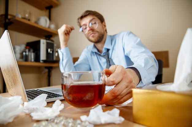 Sich krank und müde fühlen. Der Mann mit der Tasse heißen Tees, der im Büro arbeitet