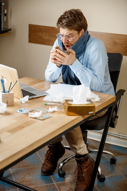 Sich krank und müde fühlen. Der Mann mit der Tasse heißen Tees, der im Büro arbeitet