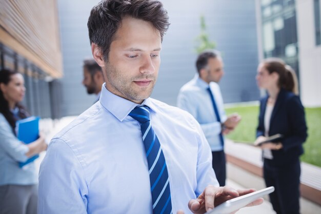 Sicherer Geschäftsmann, der digitales Tablett außerhalb des Bürogebäudes verwendet