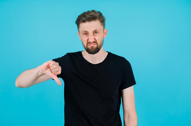 Sicherer junger Mann zeigt mit dem Daumen auf blauem Hintergrund nach unten