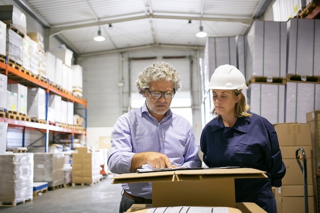 Kostenloses Foto sicherheitsinspektor berät weibliche logistikarbeiterin beim ausfüllen des formulars im lager. kopierraum, vorderansicht. arbeits- und inspektionskonzept