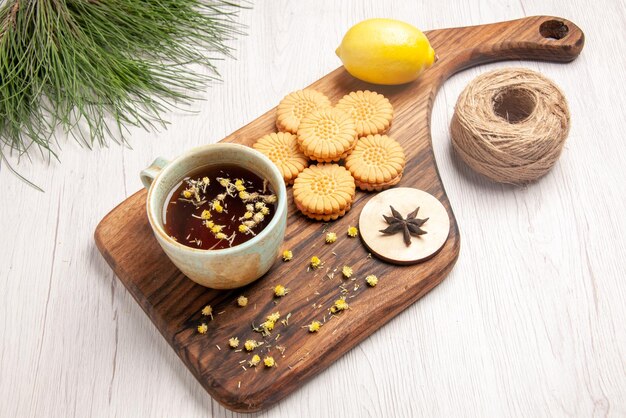 Side close-up Cookies Cookies Zitrone weiße Tasse Kräutertee Sternanis auf dem Holzbrett neben den Weihnachtsbaumzweigen