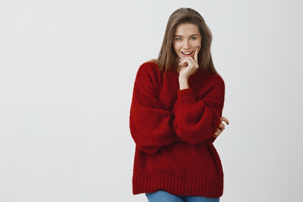 Sie weiß genau, wie verführerisch sie ist. Freche gut aussehende flirty europäische Frau im losen roten Winterpullover beißenden Finger grinsend mit interessanter Idee im Sinn vorbei