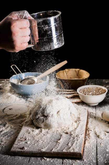 Sieb Mehl des Bäckers durch ein Sieb auf Holztisch