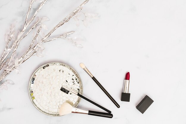 Silber- und Kristallzweig mit Platte; Make-up-Pinsel und Lippenstift auf weißem Hintergrund
