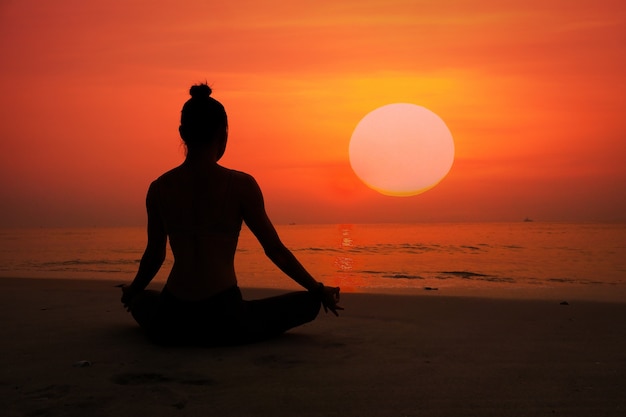 Silhouette der Frau, die Yoga auf einem Strand