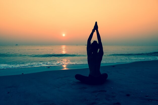 Silhouette der Frau, die Yoga auf einem Strand