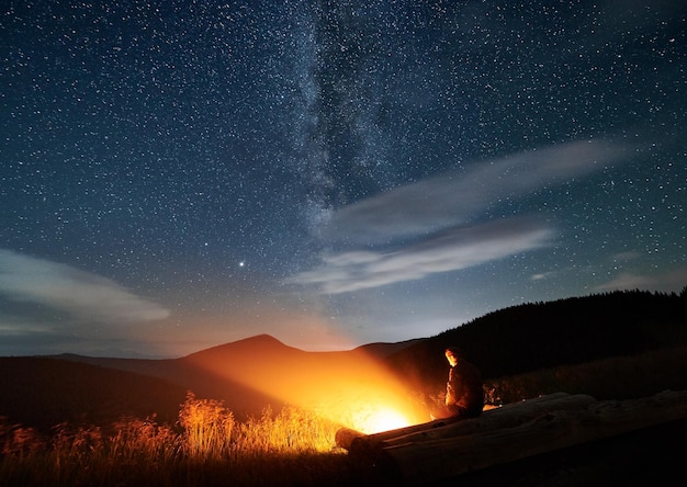 Silhouette des Mannes, der in den Bergen in der Nähe des Lagerfeuers ruht