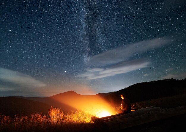 Silhouette des Mannes, der in den Bergen in der Nähe des Lagerfeuers ruht