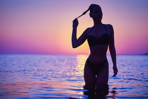 Silhouette einer sexy frau, die bei sonnenaufgang am strand posiert
