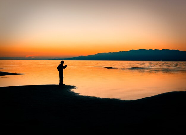 Silhouette eines Mannes, der an der Küste und dem Sonnenunterganghimmel über dem Meer steht